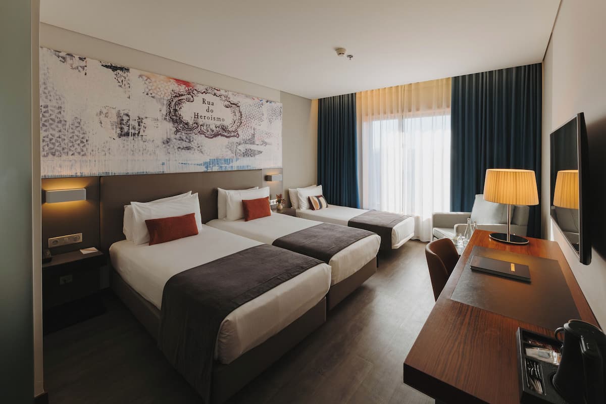 A hotel room with two beds, a desk, a chair, a TV, and a large abstract painting on the wall.