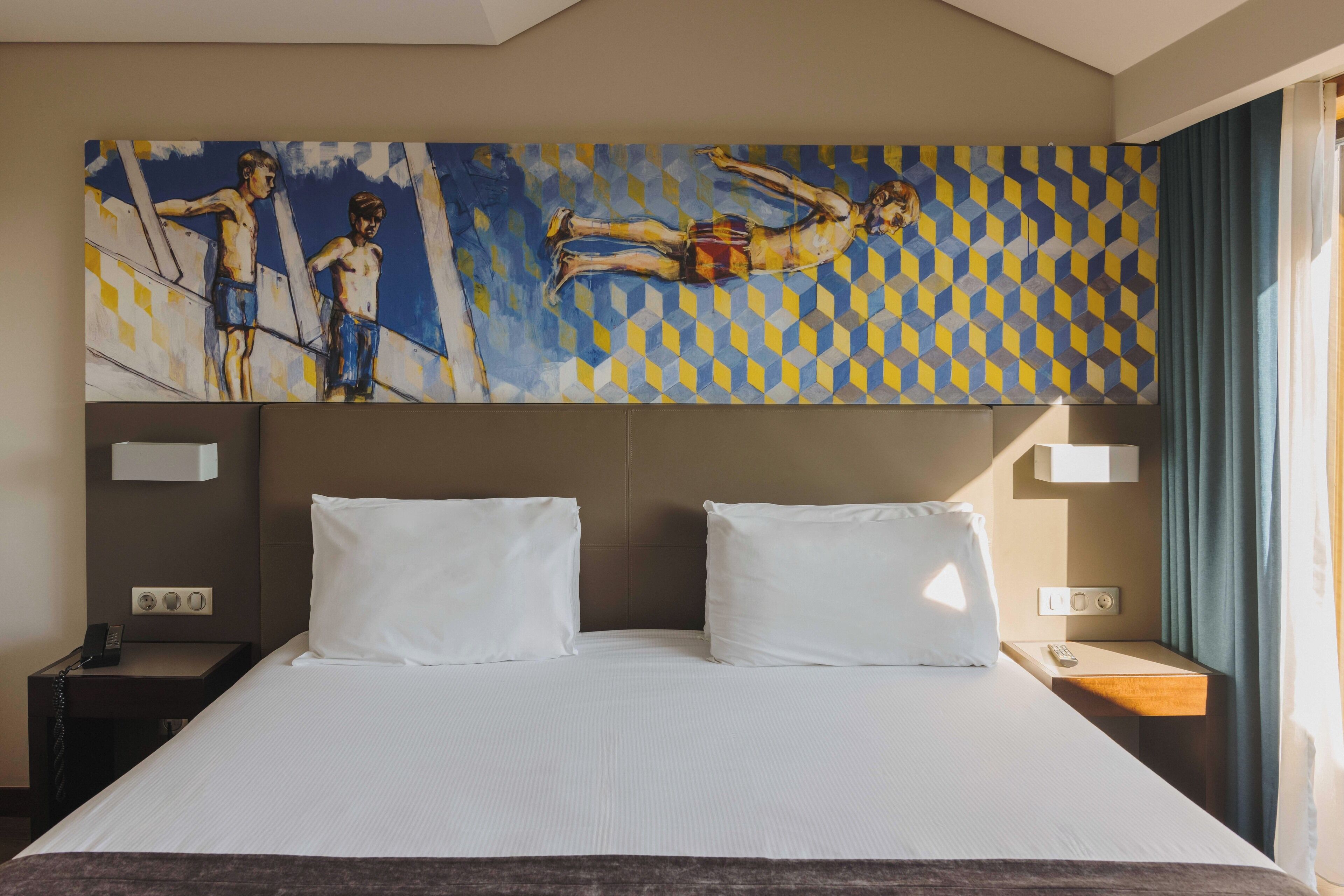 Habitación de hotel con una cama grande, dos almohadas blancas, una mesita de noche con teléfono y un cuadro sobre la cama.