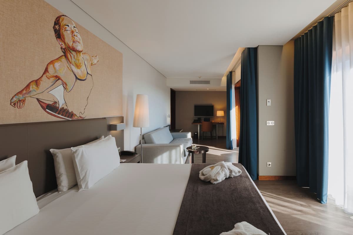 A hotel room with a large bed, a desk, a chair, a TV, and a painting on the wall.