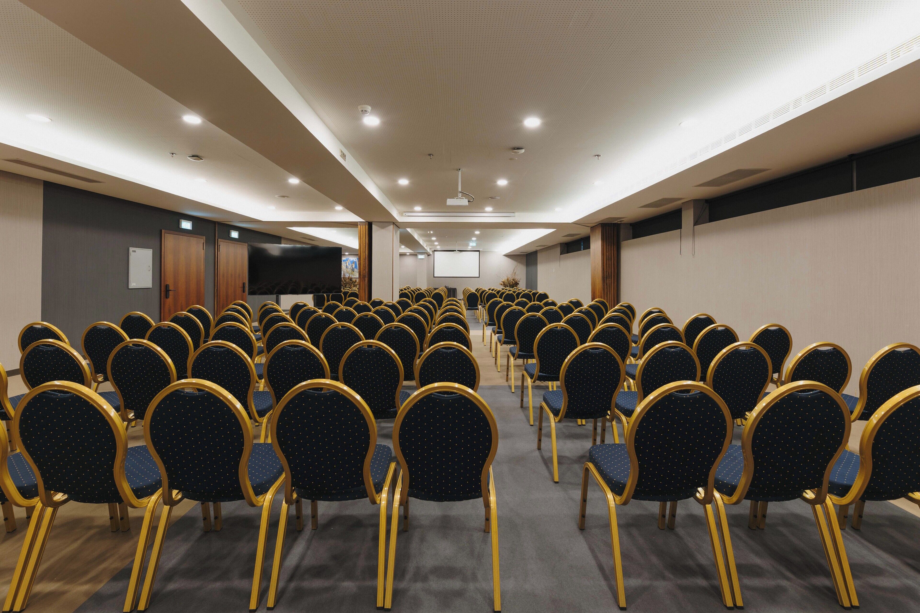 A conference room with rows of chairs and a large screen at the front.