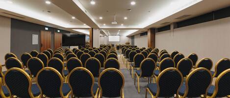 A conference room with rows of chairs and a large screen at the front.