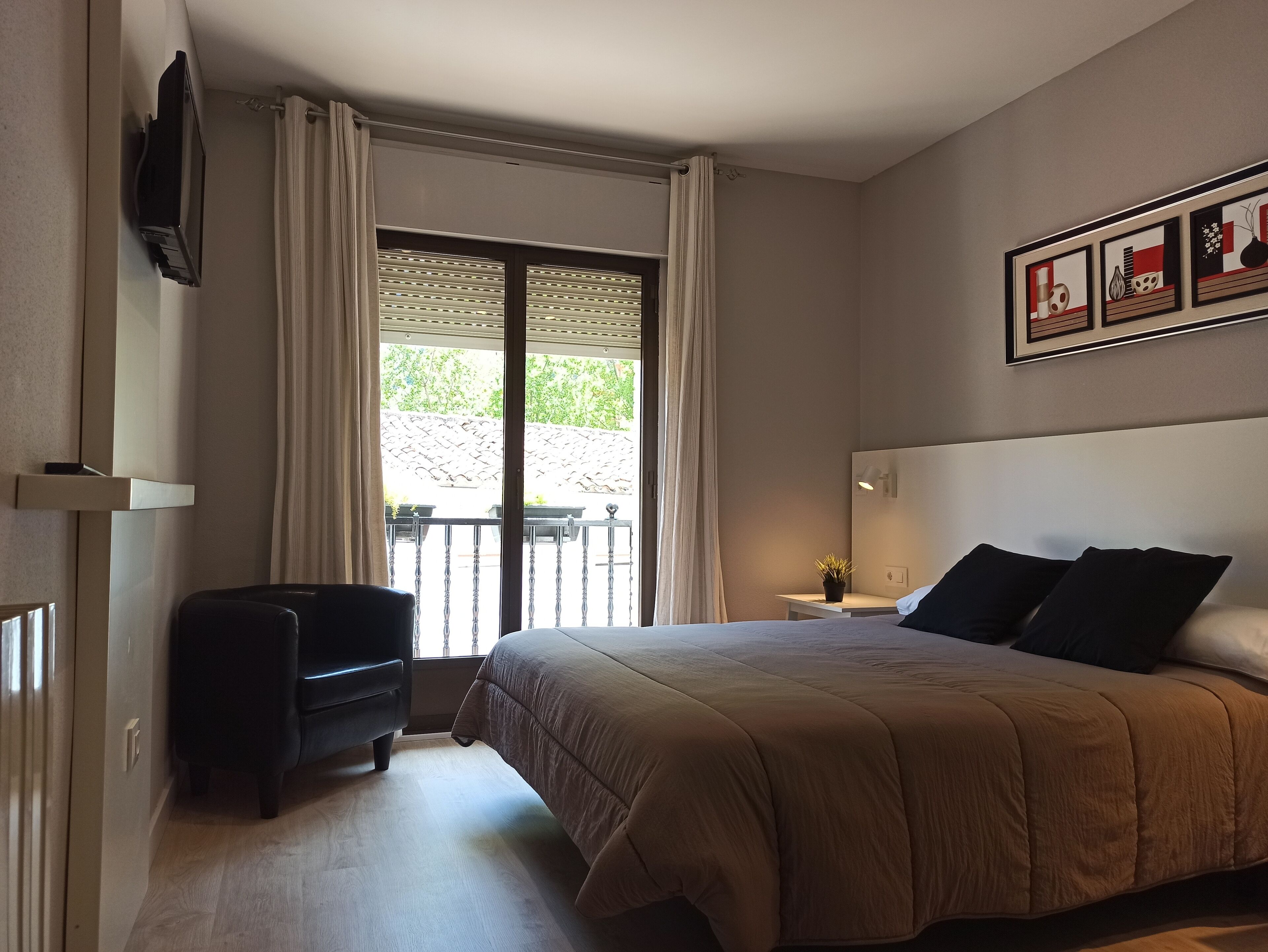 A bedroom with a bed, a chair, a TV, and a balcony with curtains.