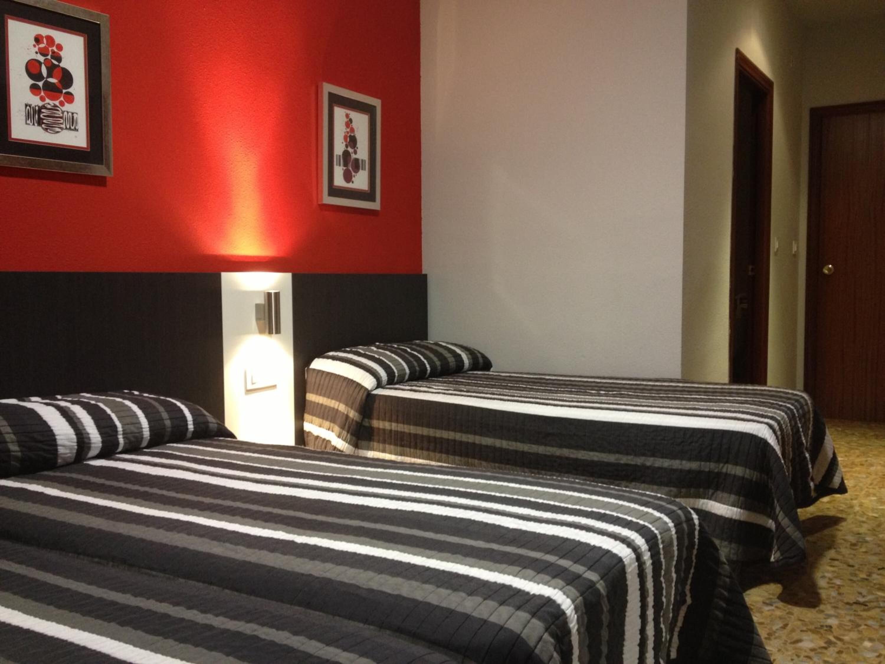 Een hotelkamer met twee bedden, een rode muur en twee ingekaderde foto's.