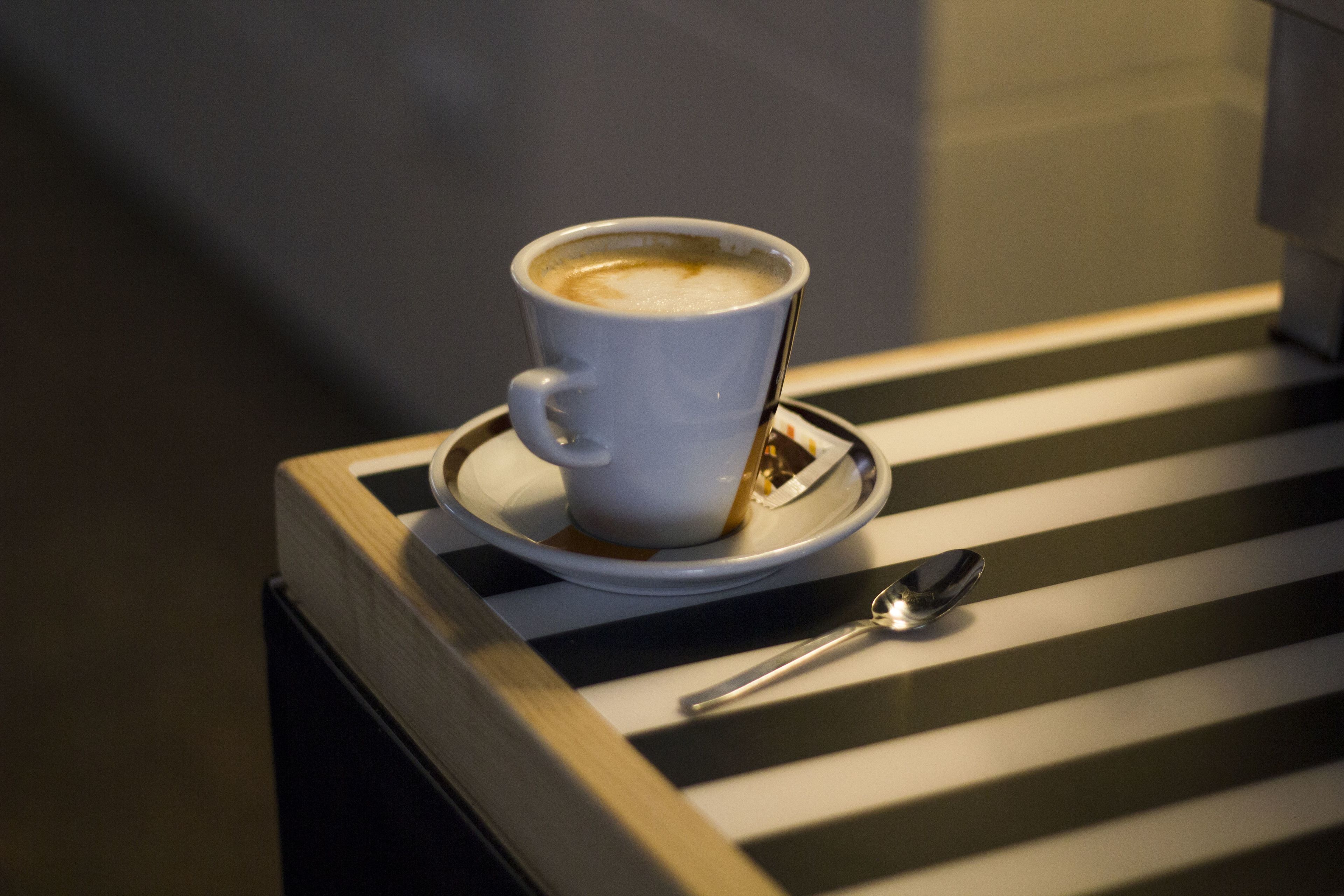 Uma chávena de café branco com uma colher sobre uma mesa listrada.