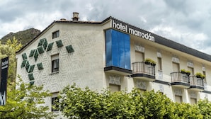 A hotel with a geometric facade, balconies with plants, and a mountainous backdrop. - Hotel Marrodan (Arnedillo)