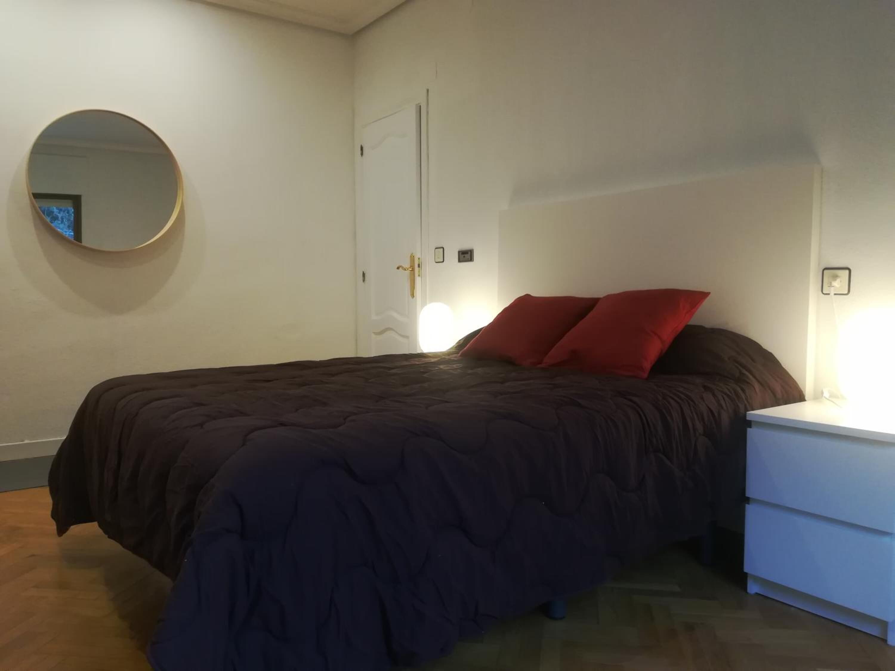 A bedroom with a bed, a nightstand, a mirror, and a door.