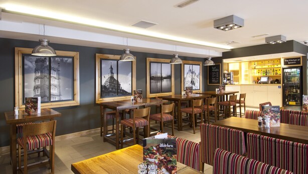 A restaurant with wooden tables and striped booths, framed pictures on the wall, and a bar area with a menu. - Premier Inn Ipswich Town Centre - Quayside (Ipswich)