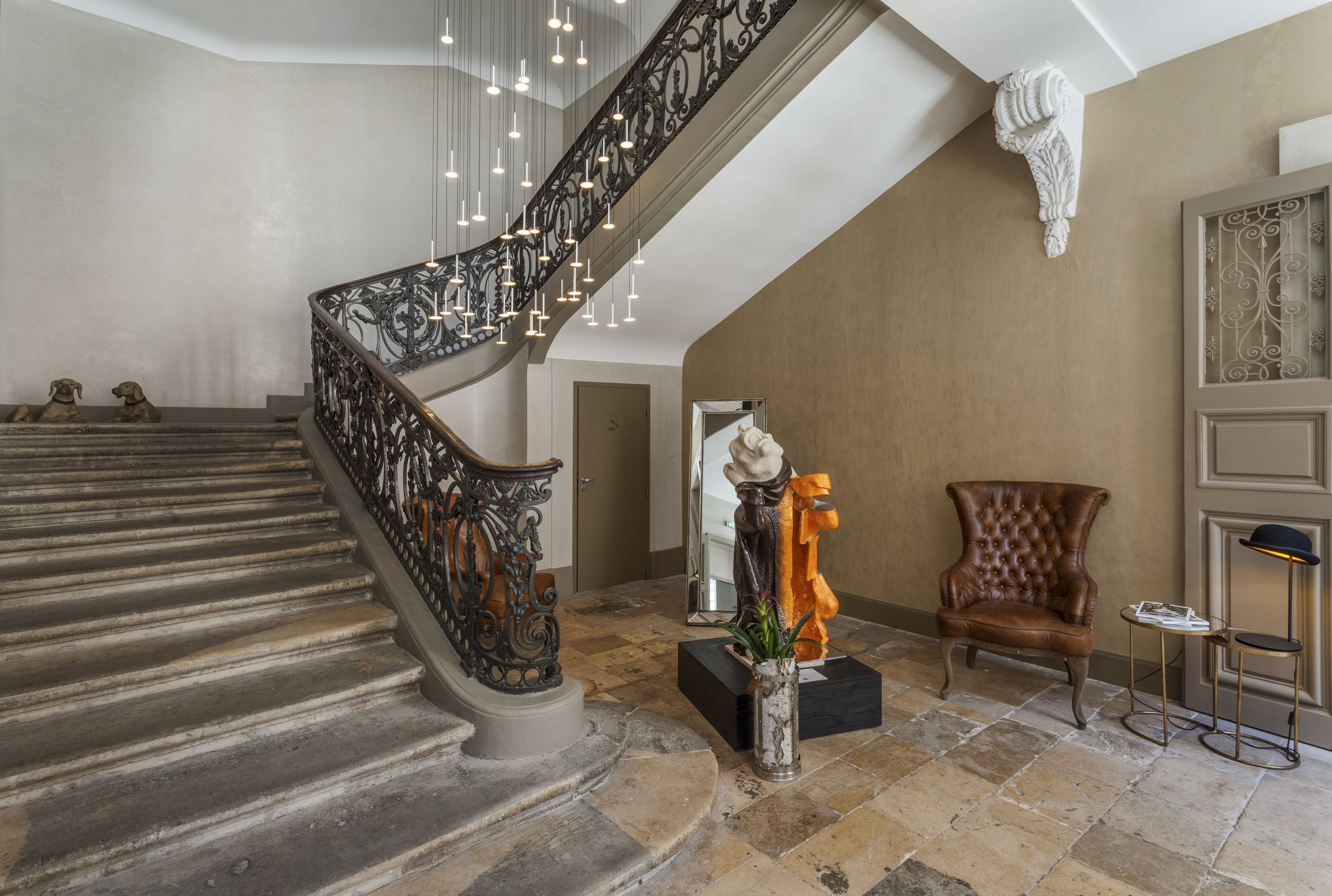 Eine prächtige Treppe mit aufwendiger Balustrade, ein großer Spiegel, ein dekorativer Sessel und eine Stehlampe.
