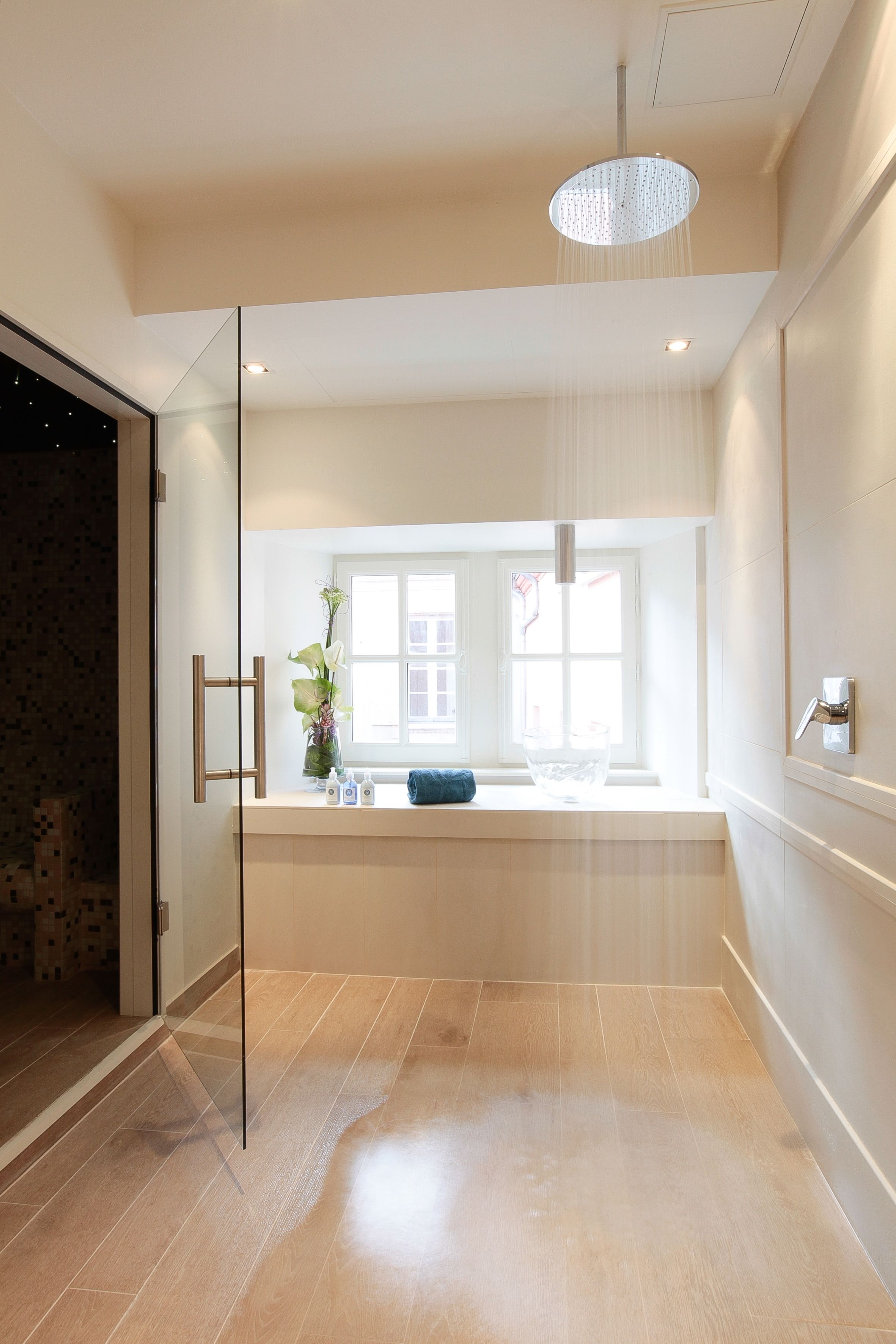 A modern bathroom with a glass shower enclosure, a large window, and a hanging light fixture.