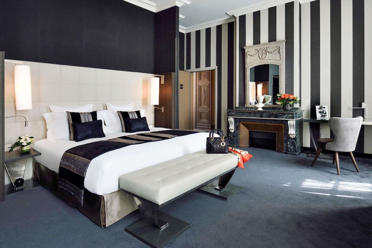 Ein modernes Hotelzimmer mit einem großen Bett, einer Bank, einem Schreibtisch, einem Sessel, einem Kamin und einem Spiegel.