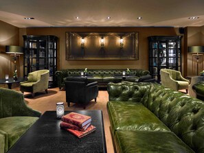 A luxurious living room with a green leather sofa, matching armchairs, a black coffee table, and a large framed artwork above the sofa. - La Cour des Consuls Hotel & Spa Toulouse - MGallery Collection (Toulouse)
