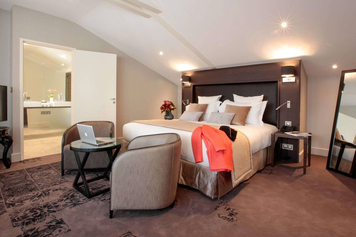 Ein modernes Hotelzimmer mit einem großen Bett, einem Schreibtisch mit einem Laptop, einem Sessel und einem kleinen Tisch.