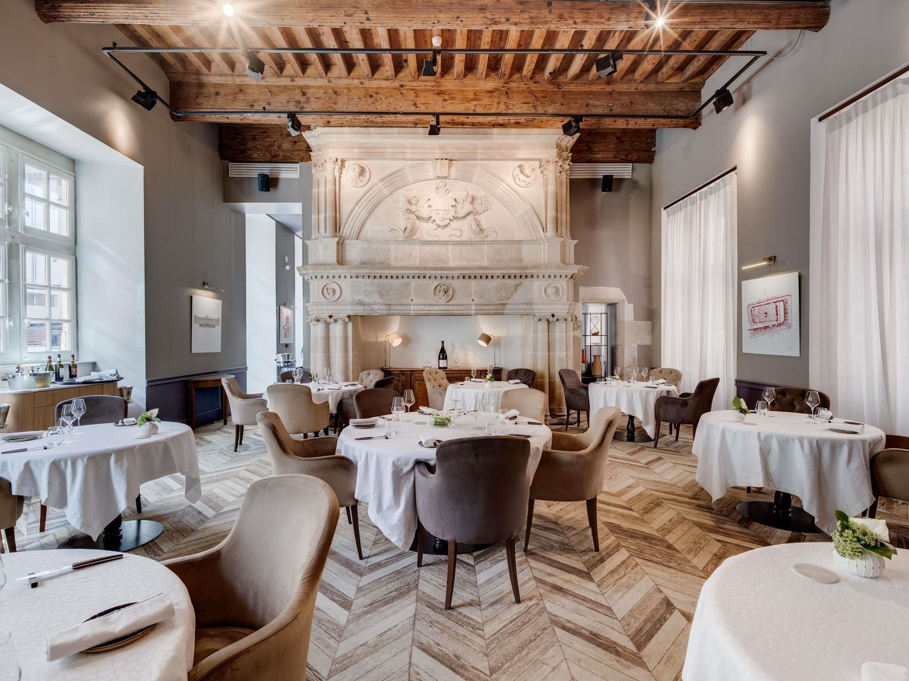 Un restaurant doté de plusieurs tables rondes, de poutres en bois au plafond et d’une cheminée décorative.