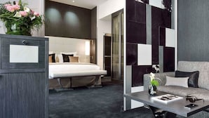 A modern hotel room with a bed, a sofa, a desk, and a large mirror. - La Cour des Consuls Hotel & Spa Toulouse - MGallery Collection (Toulouse)