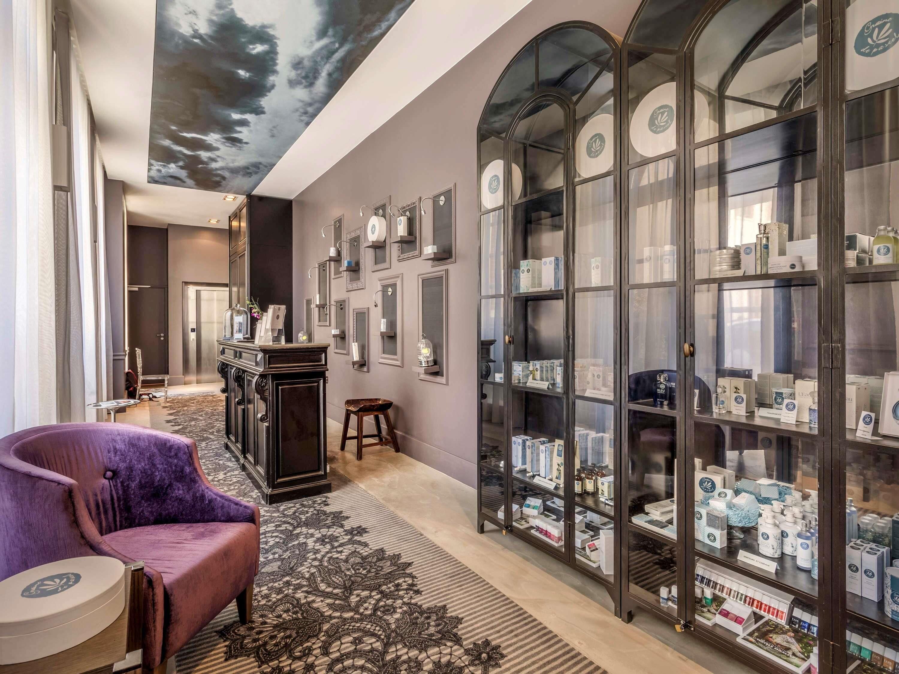 A hotel lobby with a purple armchair, a large glass display case with products, and a ceiling mural.
