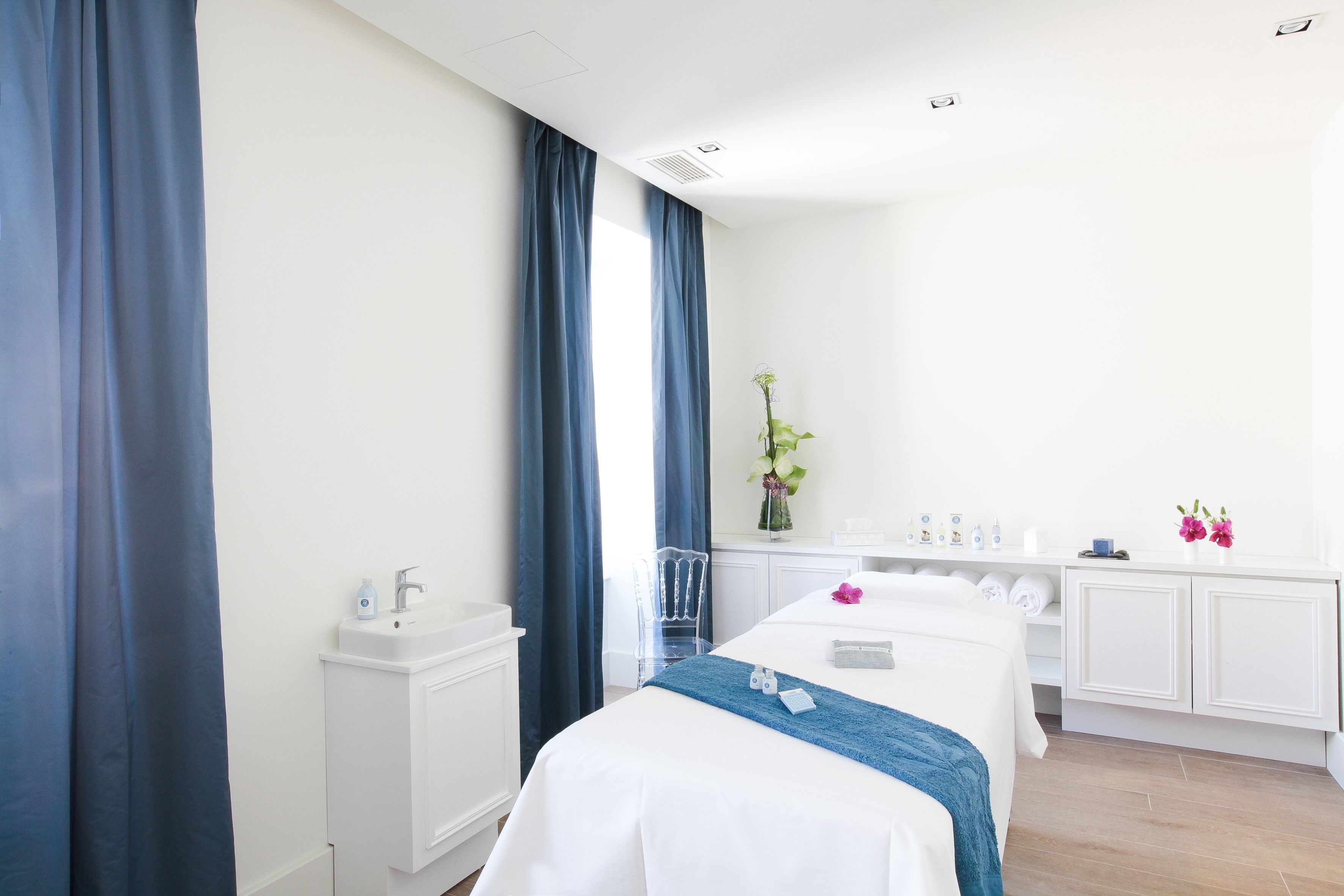 Ein Hotelzimmer mit einem Bett, einem kleinen Schreibtisch, einem Stuhl, einem Schminktisch mit Pflegeprodukten und einem Fenster mit Vorhängen.