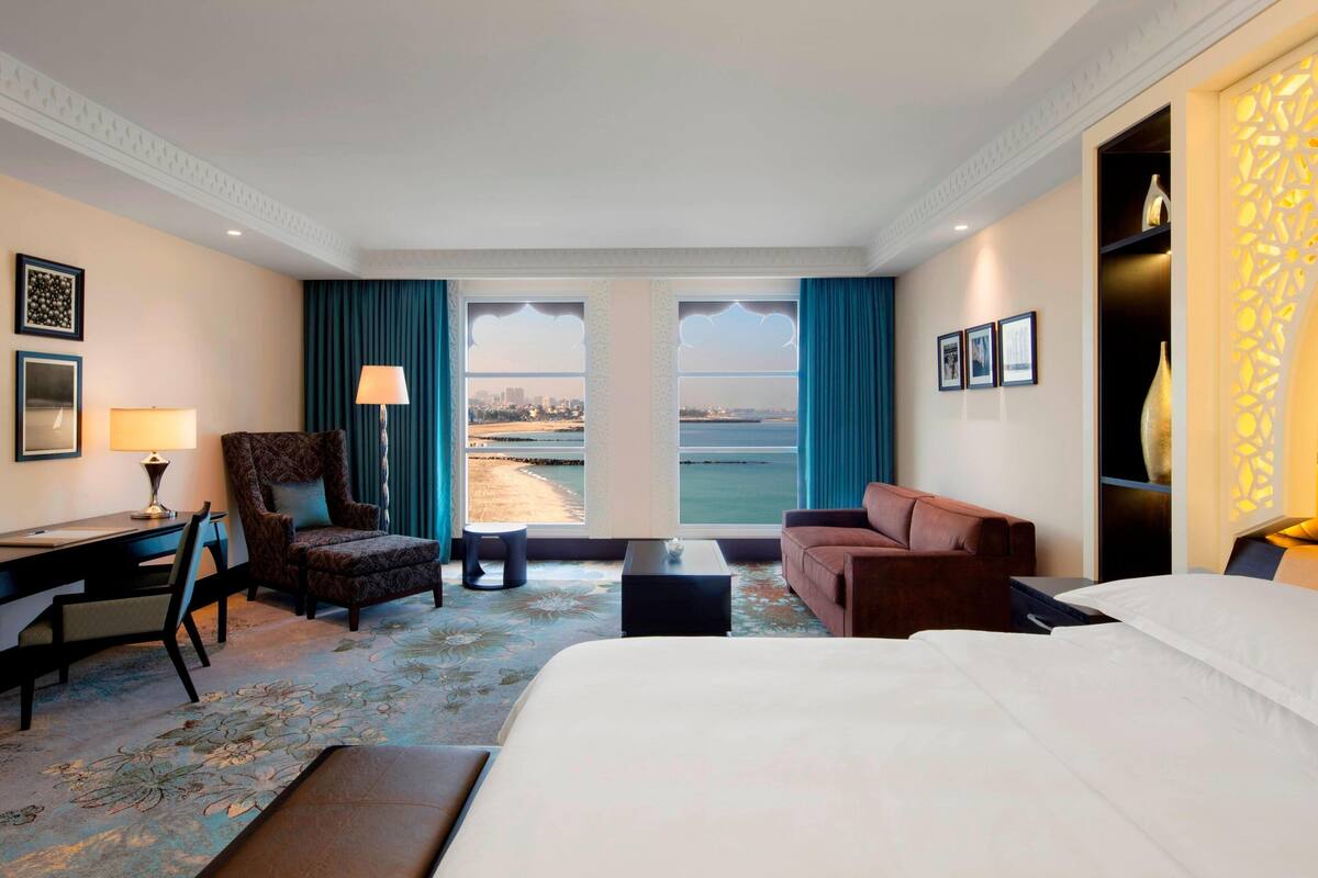 Une chambre d’hôtel avec un grand lit, un bureau, une chaise, un canapé et une vue sur la mer.