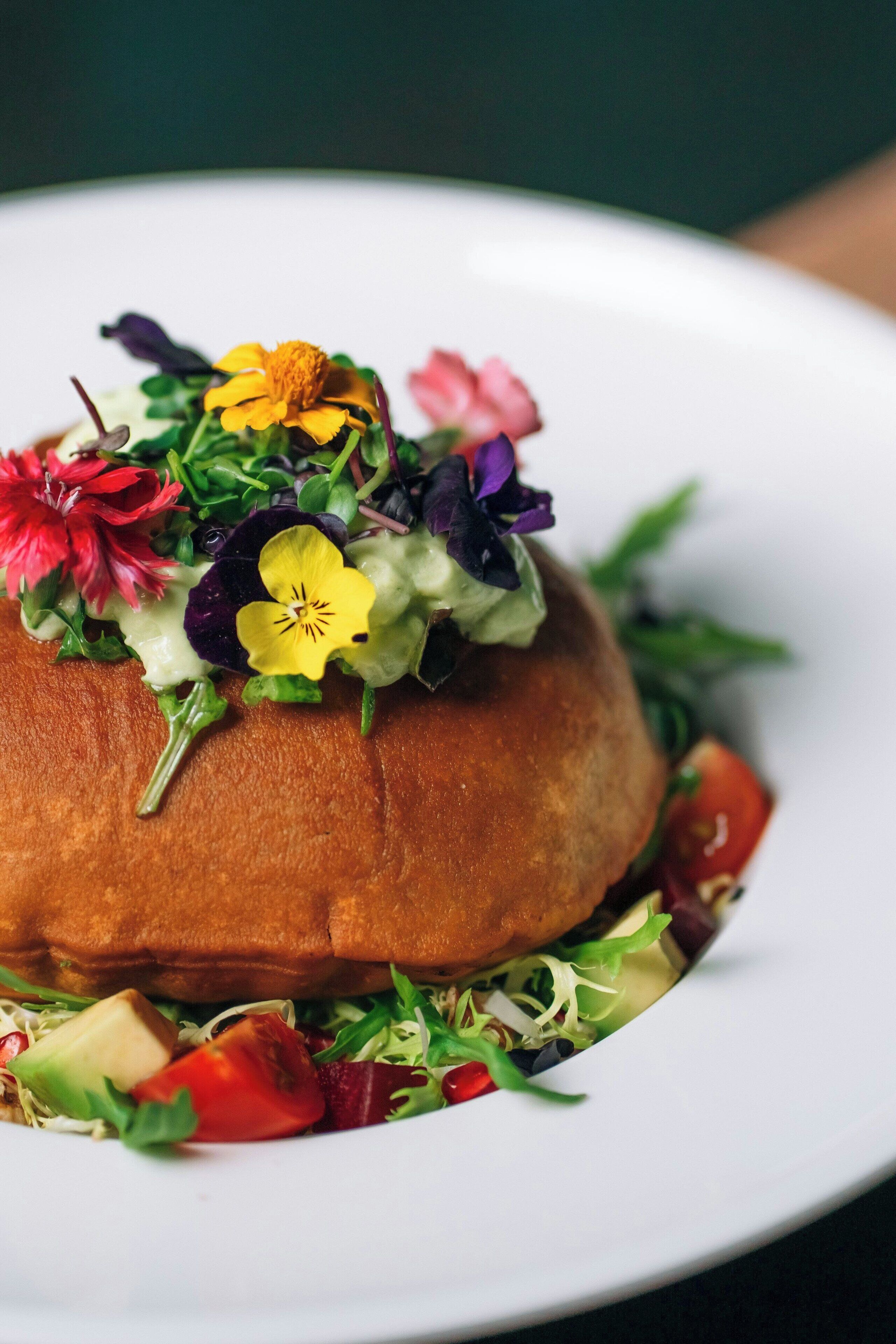 A sandwich on a white plate with various greens and flowers.