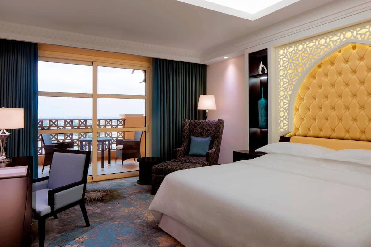 Une chambre d’hôtel avec un grand lit, une chaise, un bureau et une vue sur la mer, accessible par une porte coulissante.
