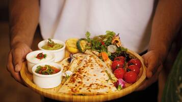 A person holding a wooden board with a quesadilla, salad, and three small bowls of dips.
