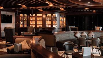 A modern lounge area with leather seating, wooden shelving with decorative items, and ambient lighting.
