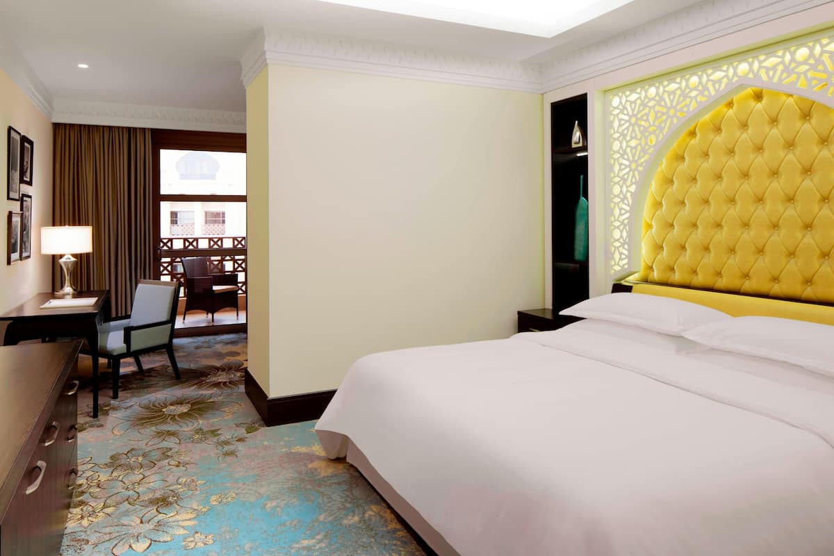 Une chambre d’hôtel avec un grand lit, un bureau avec une chaise, une fenêtre avec des rideaux et une tête de lit décorative.