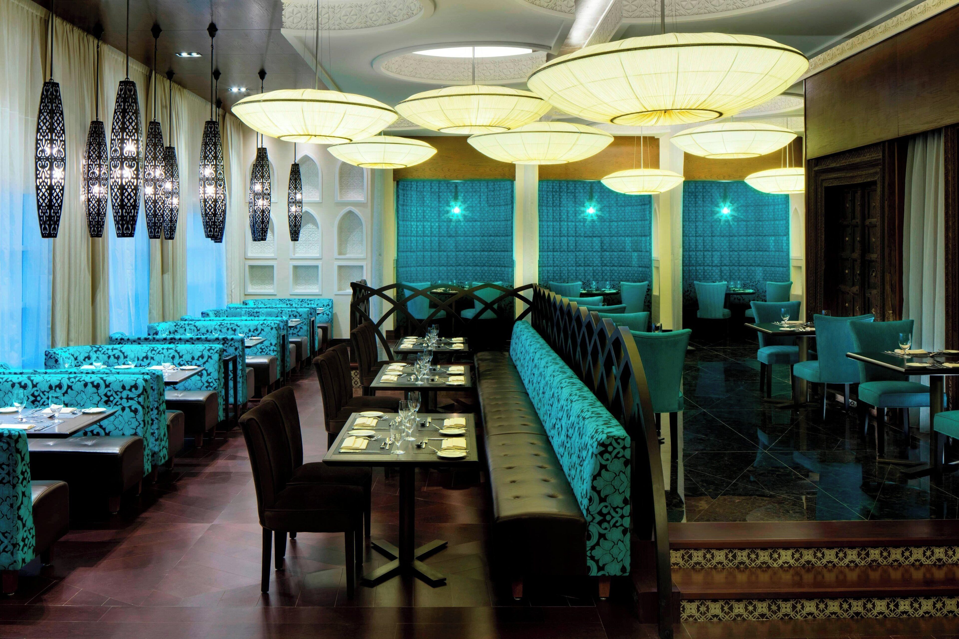 Un restaurant avec des banquettes et des tables de couleur turquoise, des lampes suspendues décoratives et un banc à motifs.