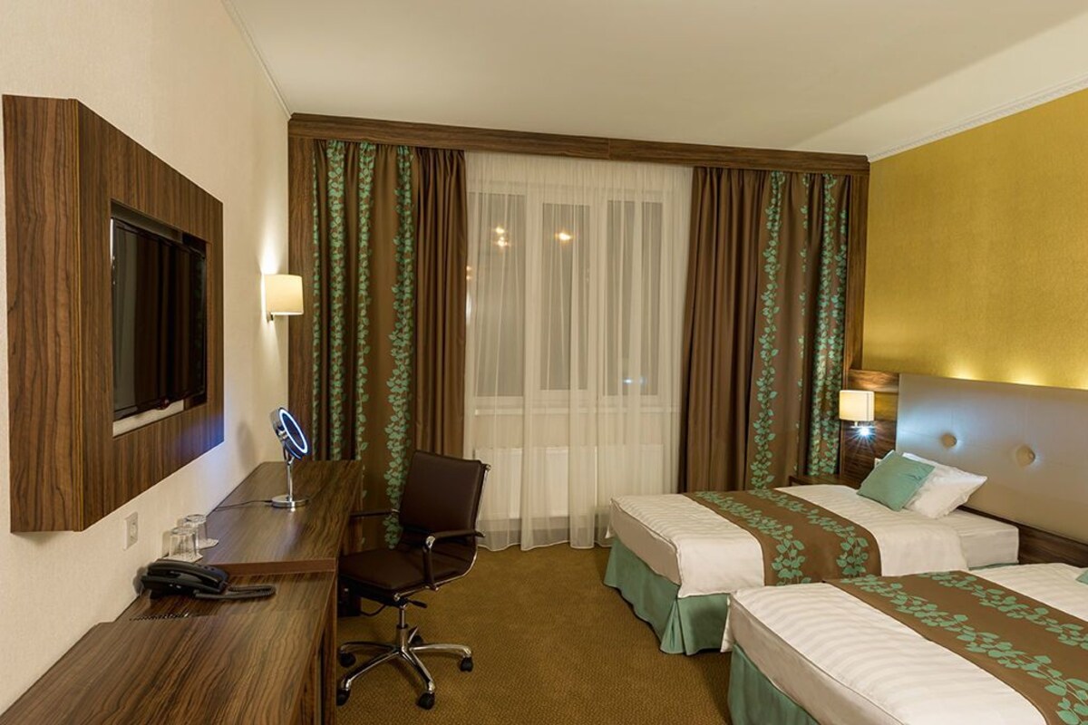 A hotel room with two beds, a desk with a chair, a TV, and a window with curtains.