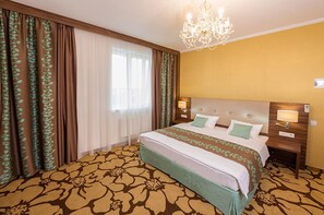 A hotel room with a large bed, a chandelier, and curtains with a leaf pattern.