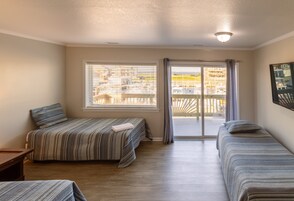 A room with two beds, a window with blinds, a door leading to a balcony, and a light fixture on the ceiling.