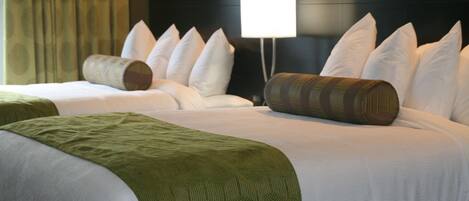 Habitación de hotel con dos camas, un cabecero grande, una lámpara de noche y una ventana con cortinas.