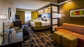 Quarto de hotel com cama, escrivaninha, cadeira, sofá e televisão.