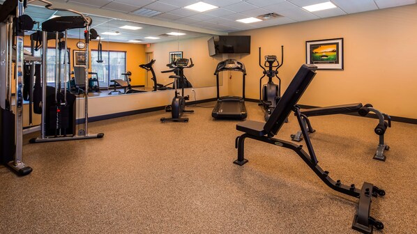 Academia com máquinas de cardio, aparelhos de musculação e um espelho grande.