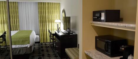 A hotel room with a bed, desk, chair, lamp, and a microwave on a shelf.