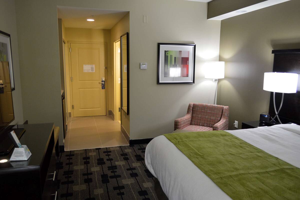 A hotel room with a bed, a chair, a desk, and a lamp.