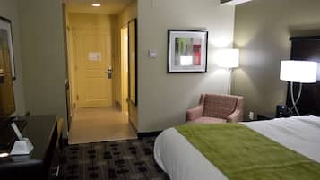 A hotel room with a bed, a chair, a desk, and a lamp.
