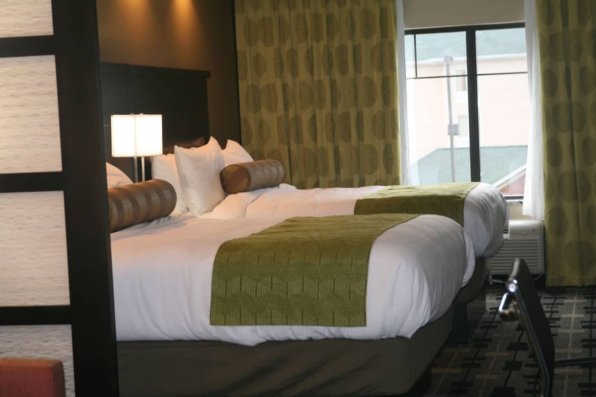 A hotel room with two beds, a large window, a view of the outside, and a lamp on the nightstand.