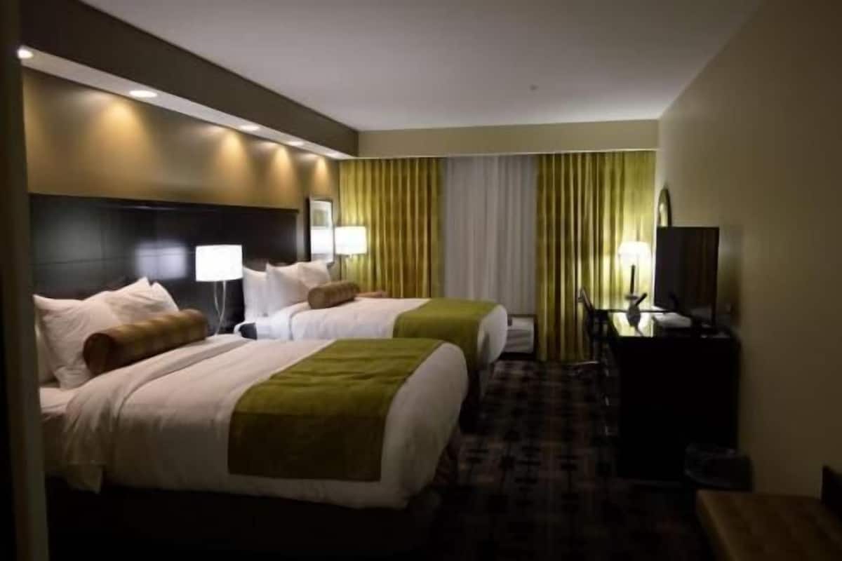 A hotel room with two beds, a desk with a lamp, and a television.