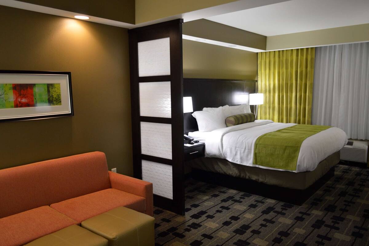 A hotel room with a bed, a nightstand, a lamp, a sofa, and a framed picture on the wall.