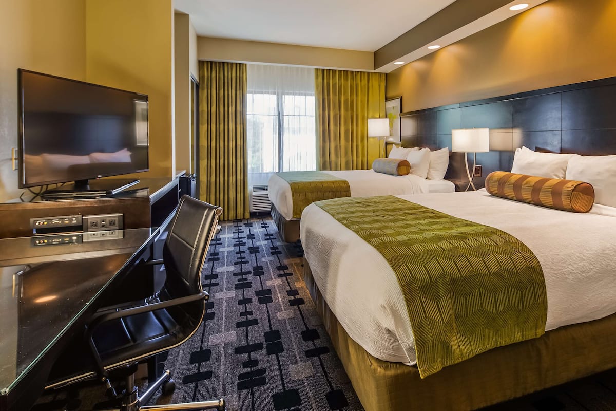 A hotel room with a bed, a desk with a TV, a chair, and a window with curtains.