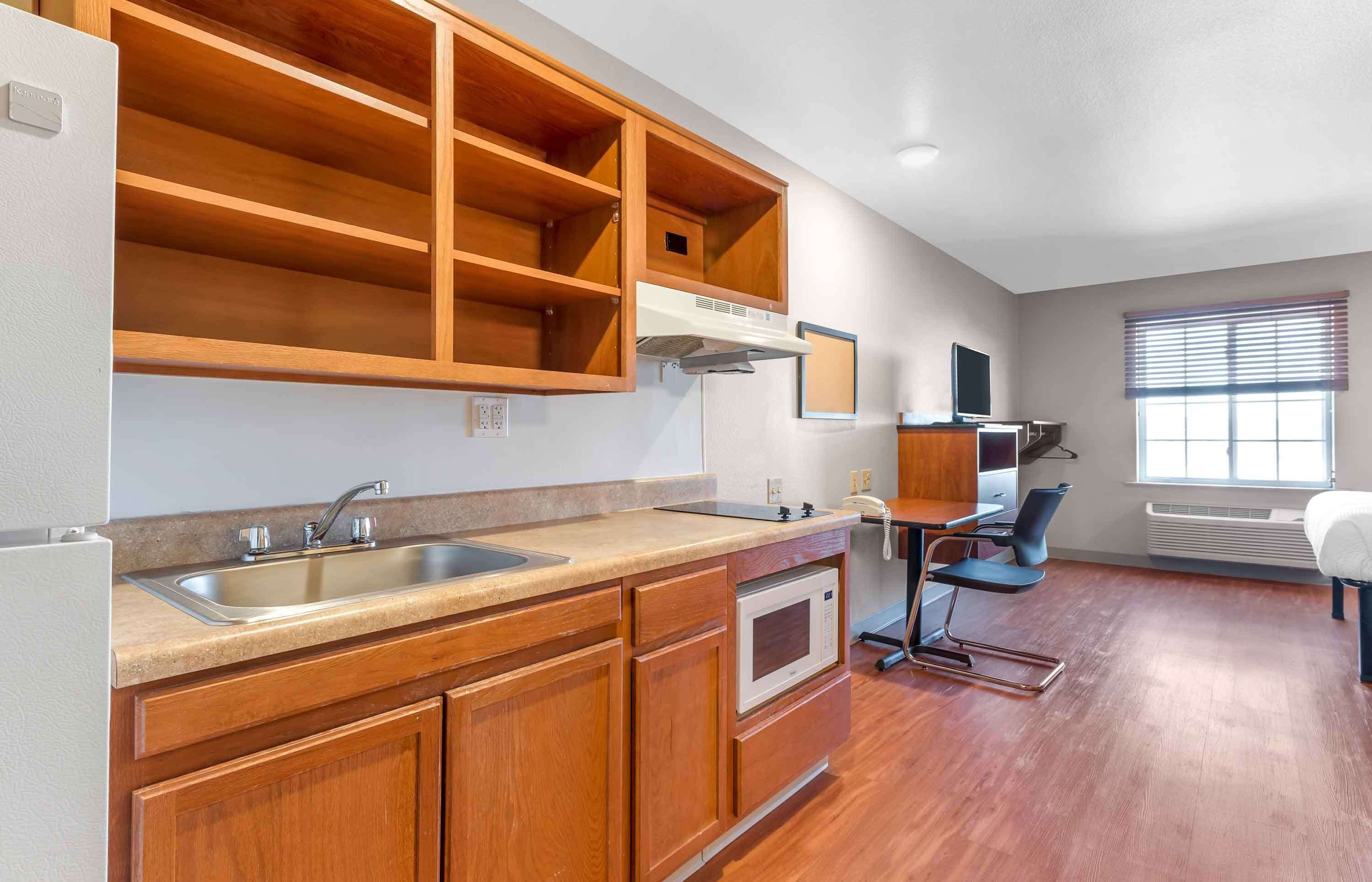 A modern kitchen with wooden cabinets, a stainless steel sink, a microwave, and a built-in range hood.