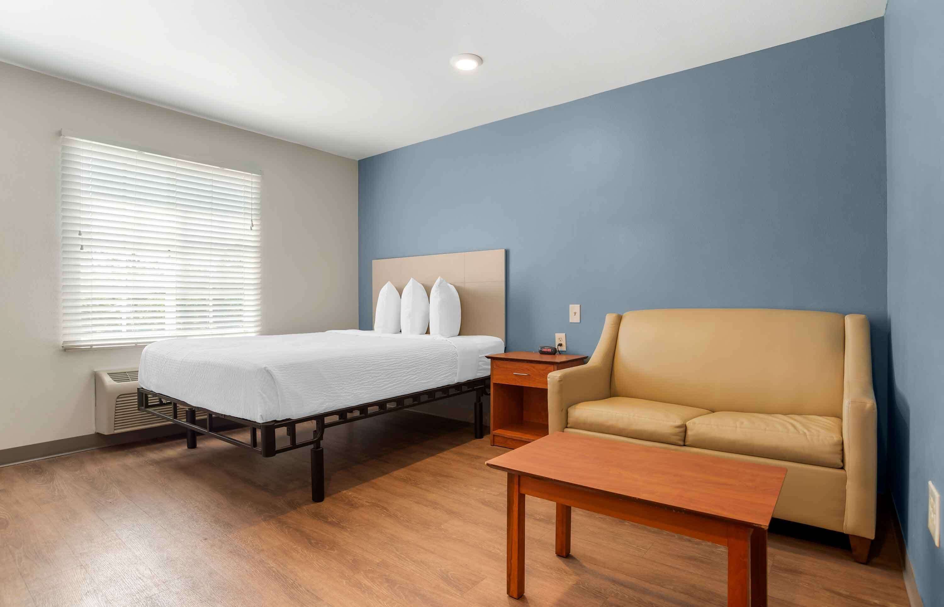 A hotel room with a bed, a sofa, a nightstand, and a wooden table.