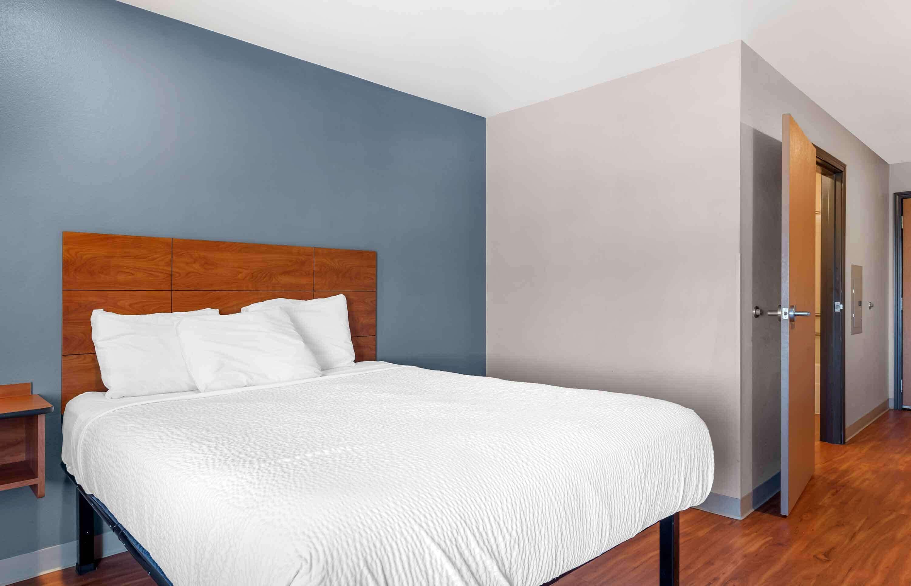 A bedroom with a wooden headboard, a white bedspread, and a nightstand.