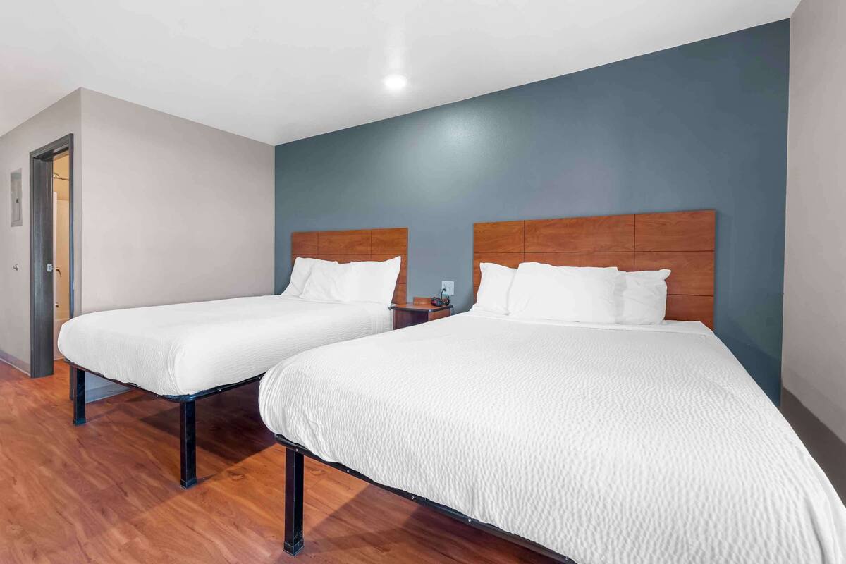 A hotel room with two beds, wooden headboards, white bedding, and a wooden floor.