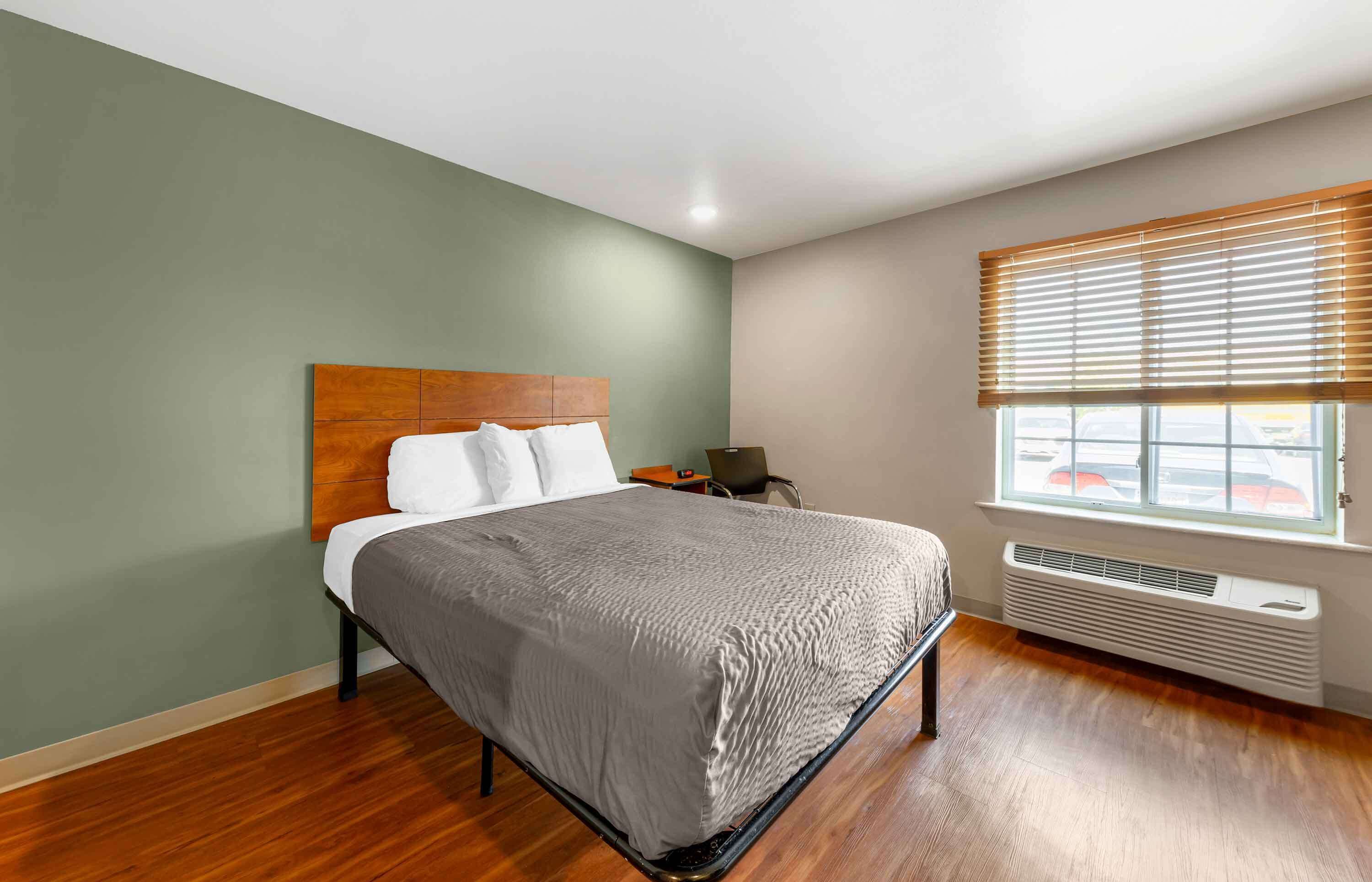 A neatly made bed with a wooden headboard, a bedside table with a lamp, and a window with blinds.