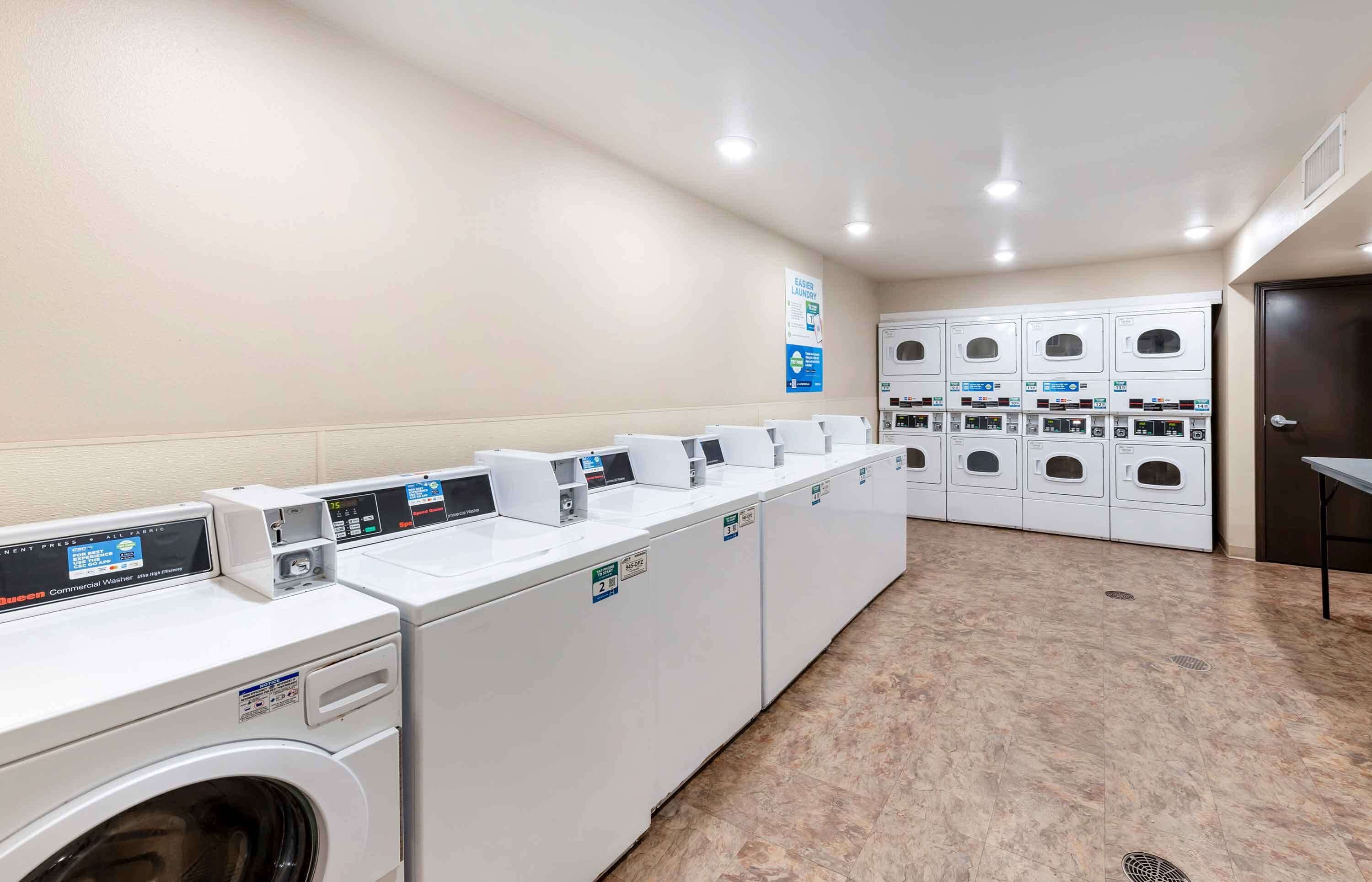 A laundry facility with multiple washing machines and dryers, a sign indicating "Easier Laundry," and a tiled floor.