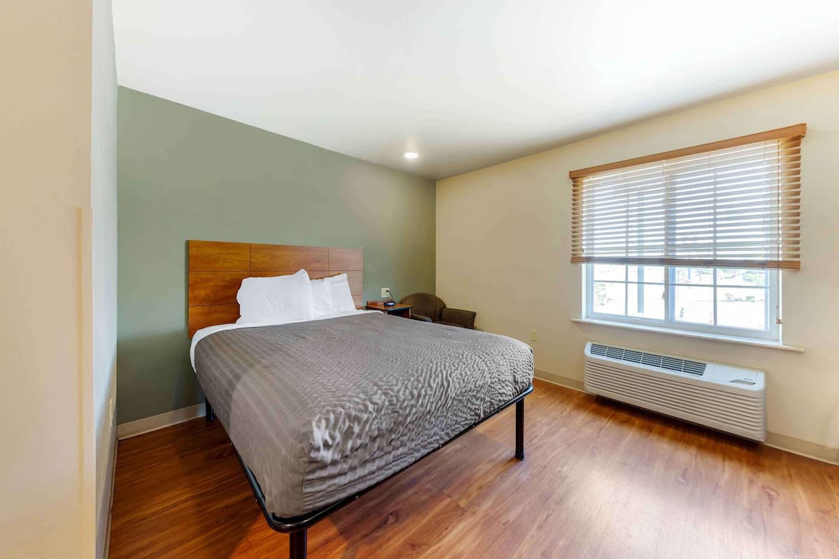 A bedroom with a bed, a window with blinds, a heater, and a wooden floor.