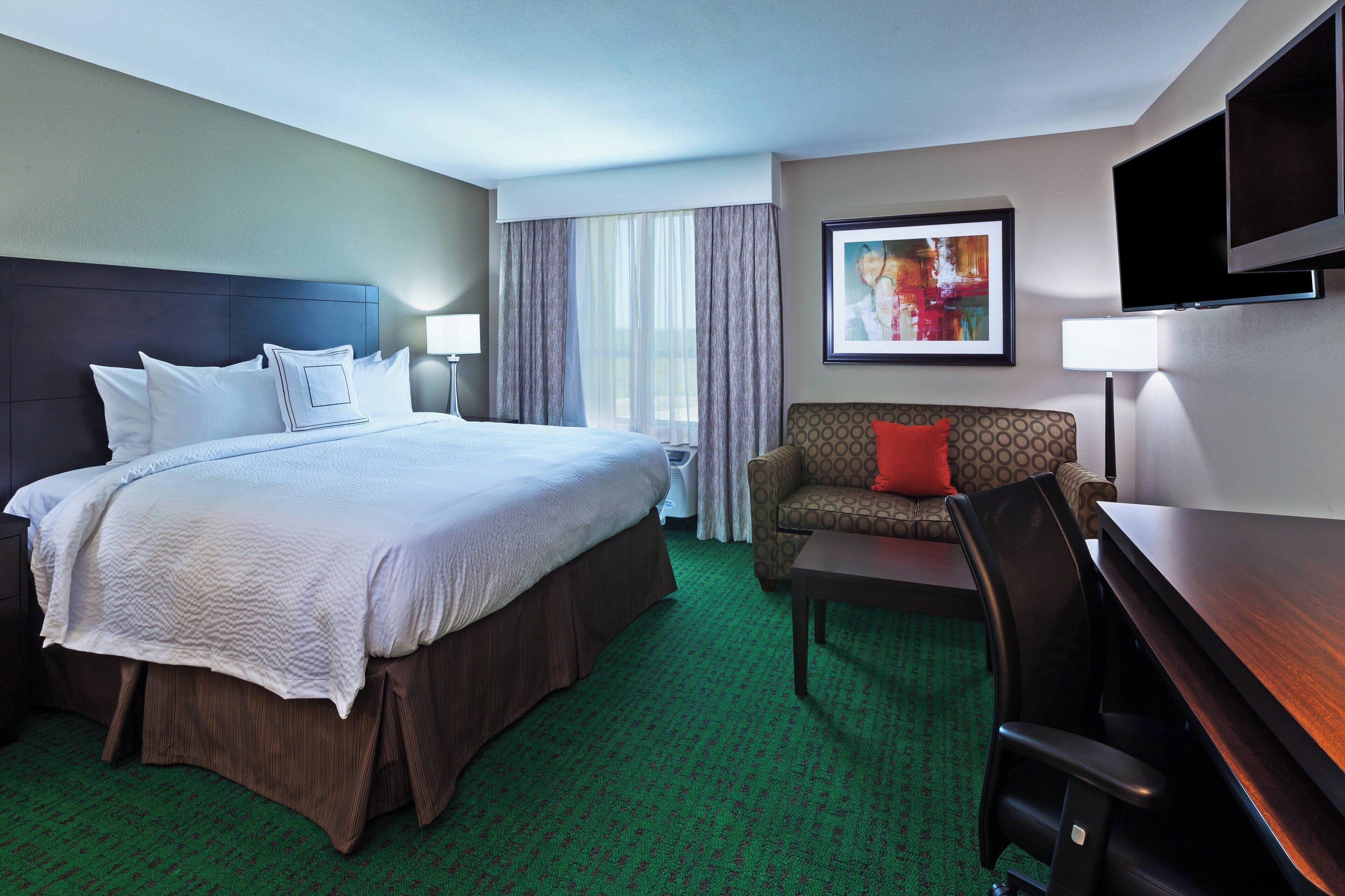 A hotel room with a large bed, a sofa, a desk, and a TV.