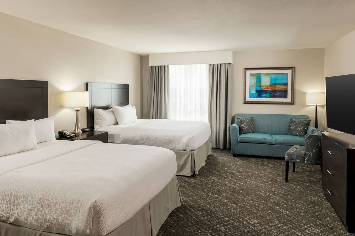 A hotel room with two beds, a sofa, a TV, and a painting on the wall.