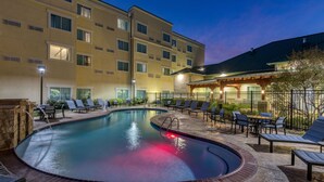 Un área de piscina de hotel con sillones de descanso y una zona de estar cubierta.